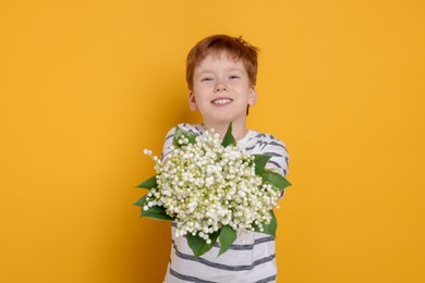 Photo of Boy with bouquet of beautiful lily-of-the-valley flowers on yellow background