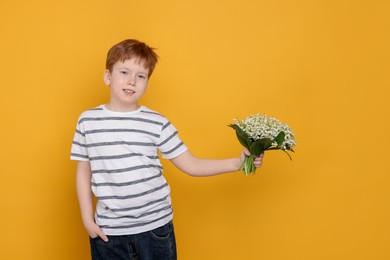 Photo of Boy with bouquet of beautiful lily-of-the-valley flowers on yellow background