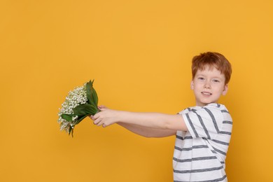 Photo of Boy with bouquet of beautiful lily-of-the-valley flowers on yellow background. Space for text