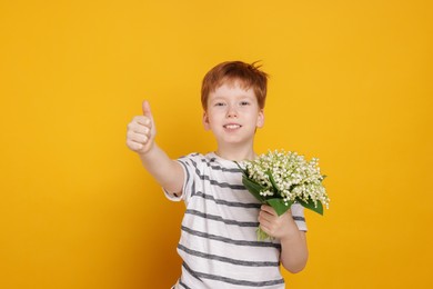 Photo of Boy with bouquet of beautiful lily-of-the-valley flowers showing thumbs up on yellow background
