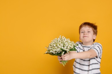 Photo of Boy with bouquet of beautiful lily-of-the-valley flowers on yellow background. Space for text