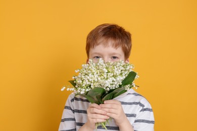 Photo of Boy with bouquet of beautiful lily-of-the-valley flowers on yellow background