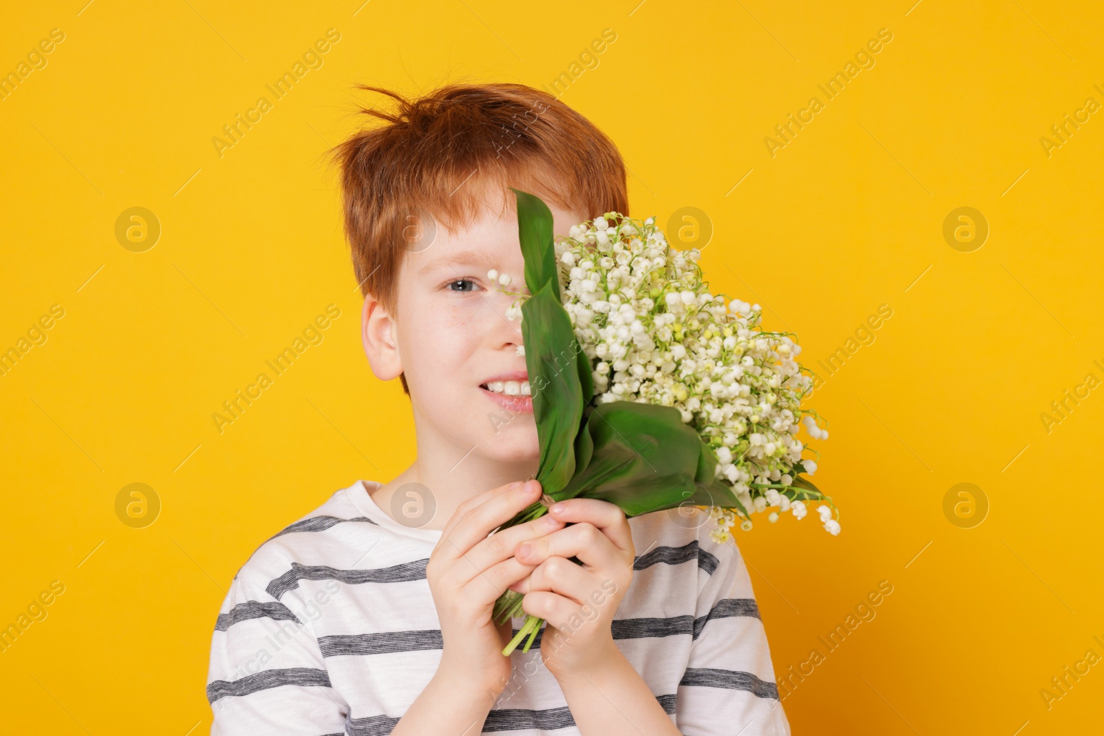 Boy with bouquet of beautiful lily-of-the-valley flowers on yellow background Photo of Boy with bouquet of beautiful lily-of-the-valley flowers on yellow background