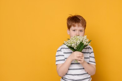 Photo of Boy with bouquet of beautiful lily-of-the-valley flowers on yellow background. Space for text