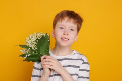 Photo of Boy with bouquet of beautiful lily-of-the-valley flowers on yellow background