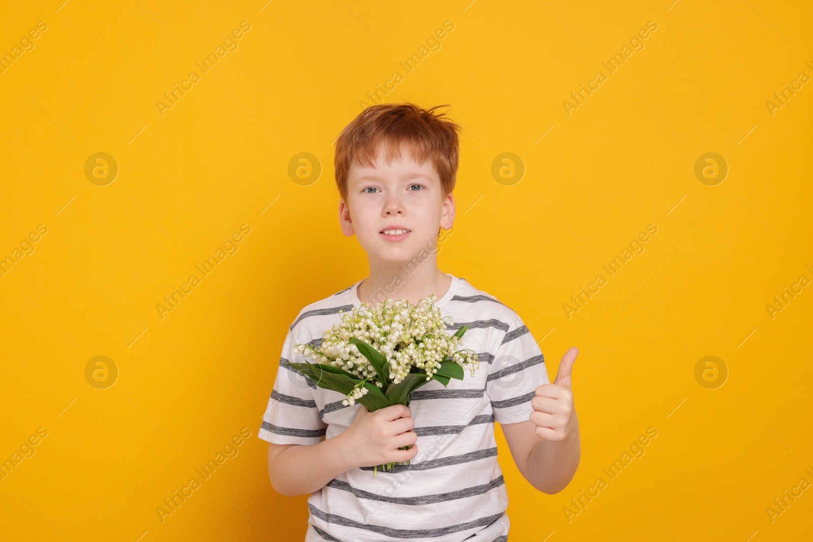 Boy with bouquet of beautiful lily-of-the-valley flowers showing thumbs up on yellow background Photo of Boy with bouquet of beautiful lily-of-the-valley flowers showing thumbs up on yellow background