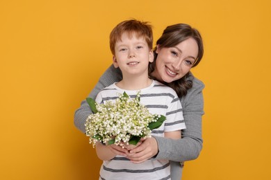 Photo of Boy giving his mother beautiful bouquet of lily-of-the-valley flowers on yellow background