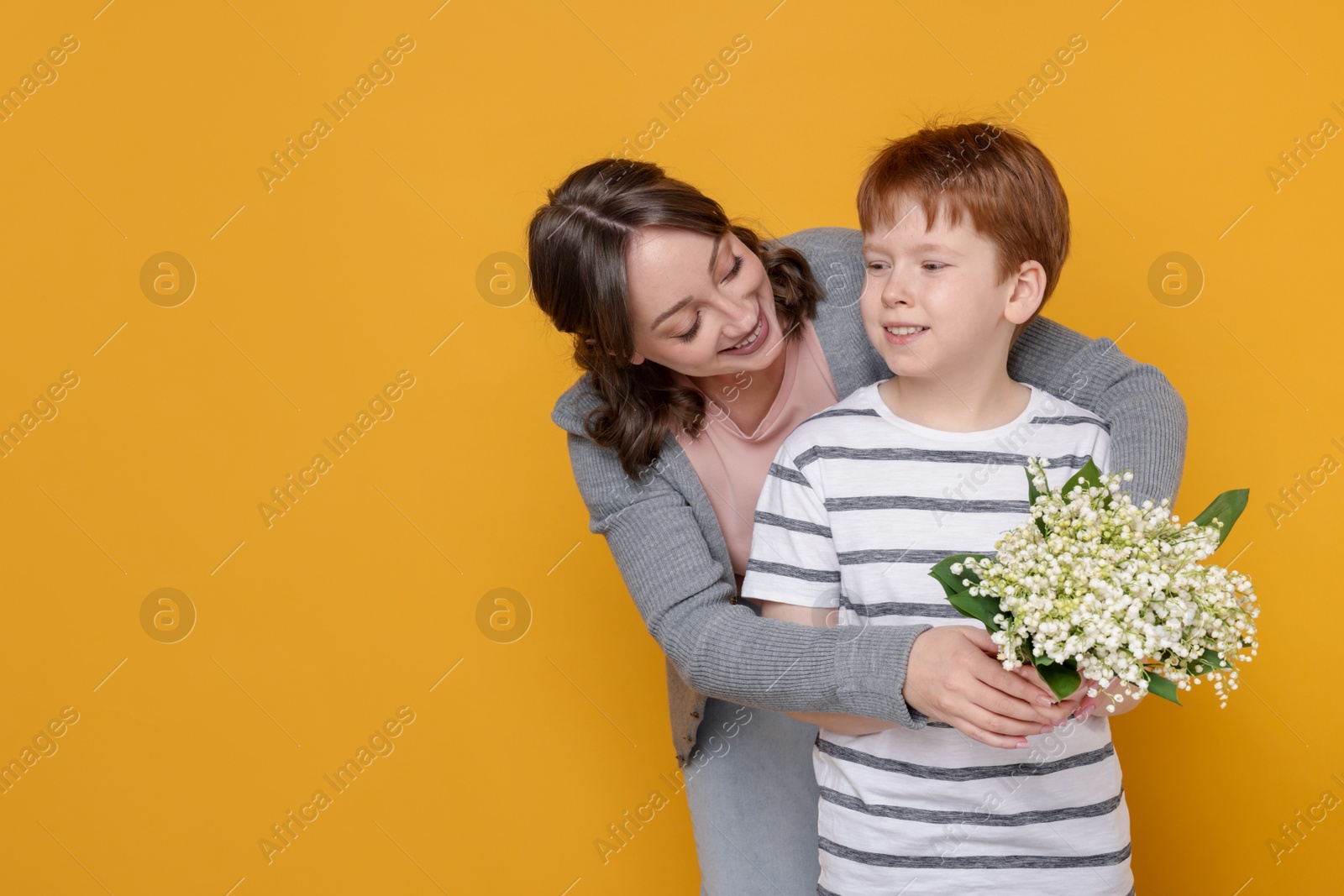 Boy giving his mother beautiful bouquet of lily-of-the-valley flowers on yellow background. Space for text Photo of Boy giving his mother beautiful bouquet of lily-of-the-valley flowers on yellow background. Space for text