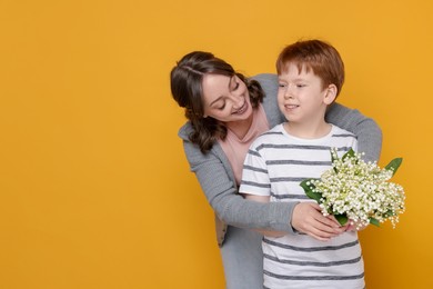 Photo of Boy giving his mother beautiful bouquet of lily-of-the-valley flowers on yellow background. Space for text