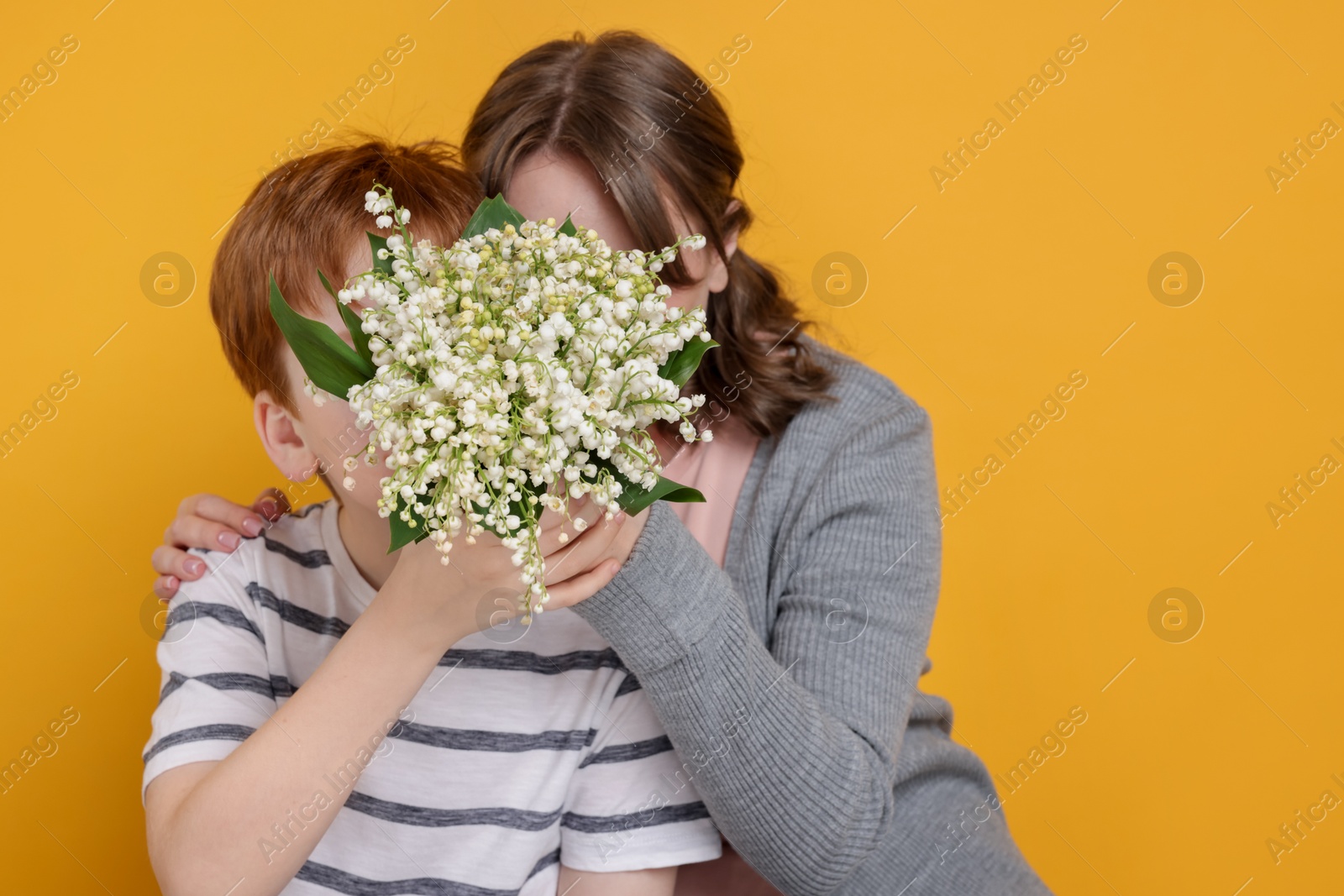 Boy giving his mother beautiful bouquet of lily-of-the-valley flowers on yellow background Photo of Boy giving his mother beautiful bouquet of lily-of-the-valley flowers on yellow background