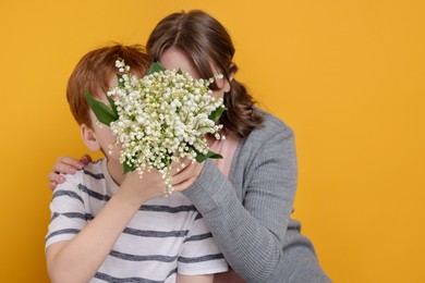 Photo of Boy giving his mother beautiful bouquet of lily-of-the-valley flowers on yellow background