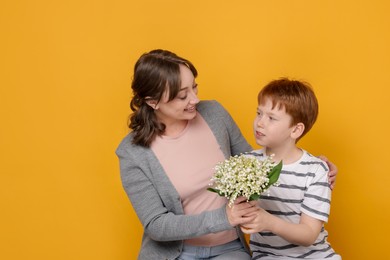 Photo of Boy giving his mother beautiful bouquet of lily-of-the-valley flowers on yellow background