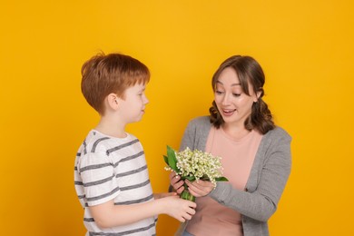 Photo of Boy giving his mother beautiful bouquet of lily-of-the-valley flowers on yellow background