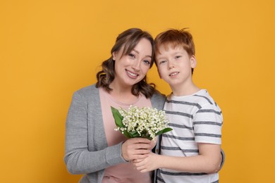 Photo of Boy giving his mother beautiful bouquet of lily-of-the-valley flowers on yellow background