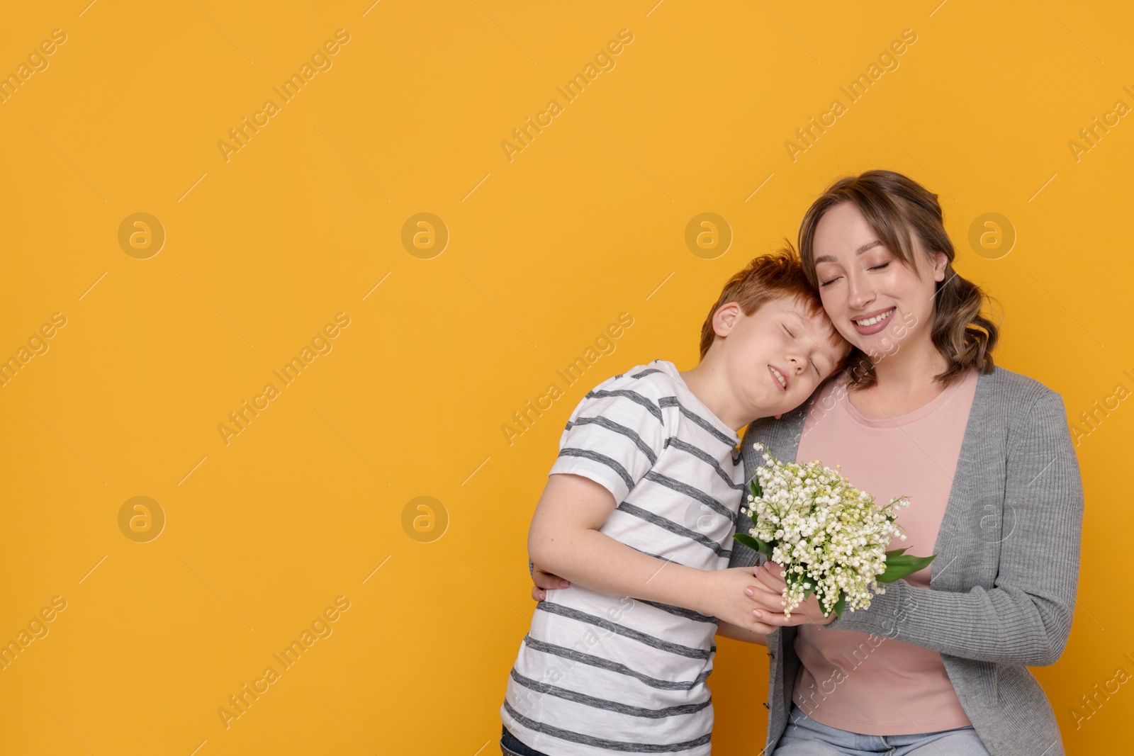 Boy giving his mother beautiful bouquet of lily-of-the-valley flowers on yellow background. Space for text Photo of Boy giving his mother beautiful bouquet of lily-of-the-valley flowers on yellow background. Space for text