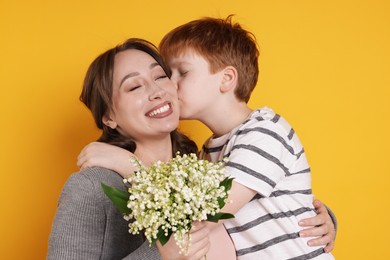Photo of Boy kissing his mother and giving beautiful bouquet of lily-of-the-valley flowers on yellow background