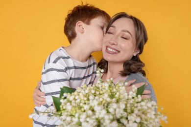 Photo of Boy kissing his mother and giving beautiful bouquet of lily-of-the-valley flowers on yellow background