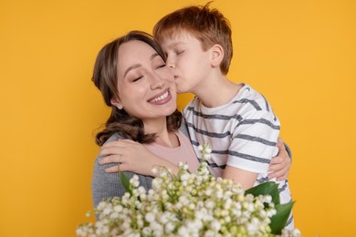 Photo of Boy kissing his mother and giving beautiful bouquet of lily-of-the-valley flowers on yellow background