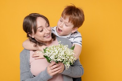 Photo of Boy giving his mother beautiful bouquet of lily-of-the-valley flowers on yellow background