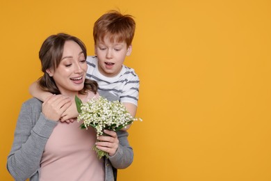 Photo of Boy giving his mother beautiful bouquet of lily-of-the-valley flowers on yellow background. Space for text