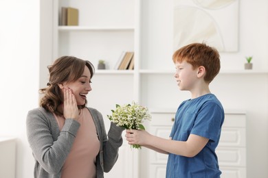 Photo of Boy surprising his mother with beautiful bouquet of lily-of-the-valley flowers at home