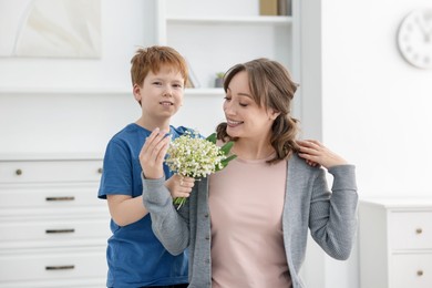 Photo of Boy giving his mother beautiful bouquet of lily-of-the-valley flowers at home
