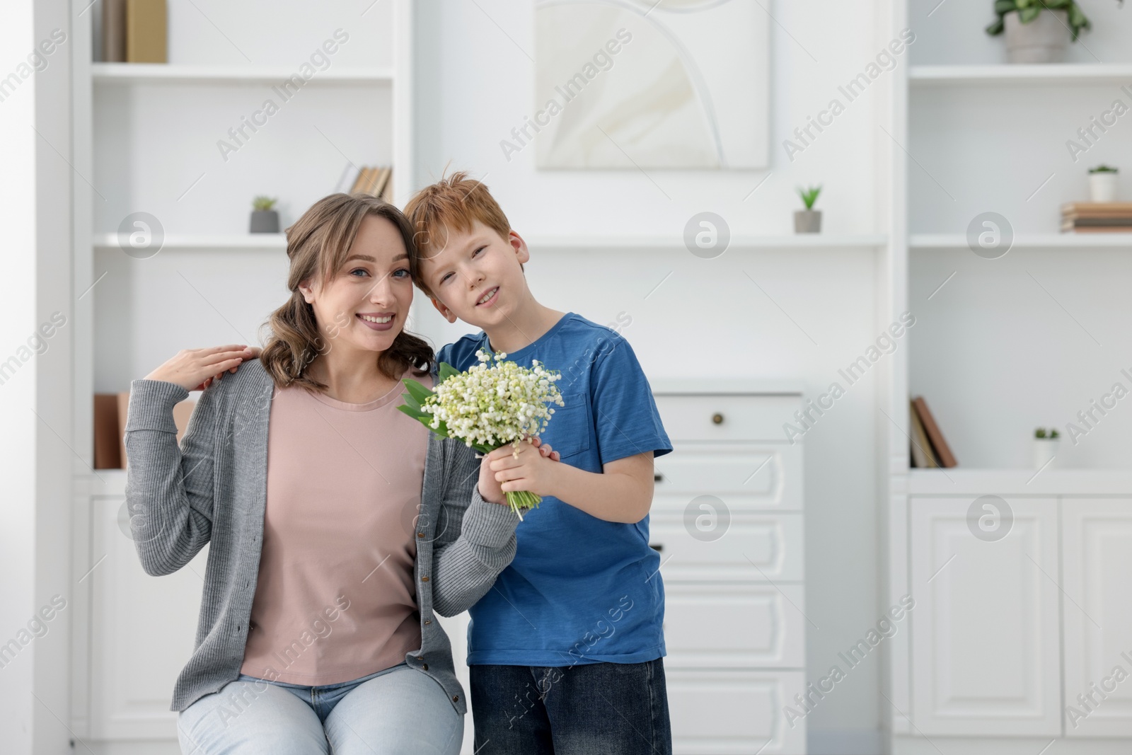 Boy giving his mother beautiful bouquet of lily-of-the-valley flowers at home. Space for text Photo of Boy giving his mother beautiful bouquet of lily-of-the-valley flowers at home. Space for text