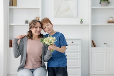 Photo of Boy giving his mother beautiful bouquet of lily-of-the-valley flowers at home. Space for text