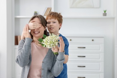 Photo of Boy surprising his mother with beautiful bouquet of lily-of-the-valley flowers at home
