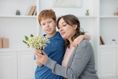 Photo of Boy giving his mother beautiful bouquet of lily-of-the-valley flowers at home
