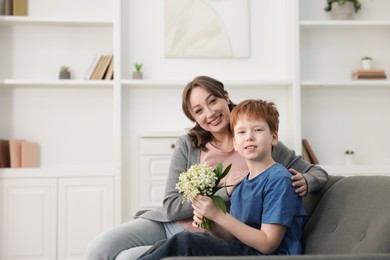 Photo of Boy giving his mother beautiful bouquet of lily-of-the-valley flowers at home. Space for text