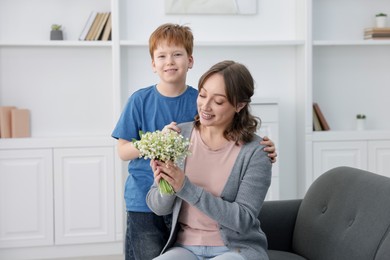 Photo of Boy giving his mother beautiful bouquet of lily-of-the-valley flowers at home