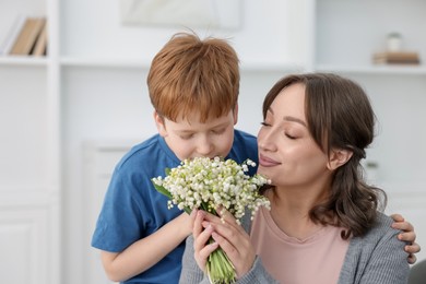 Photo of Boy giving his mother beautiful bouquet of lily-of-the-valley flowers at home