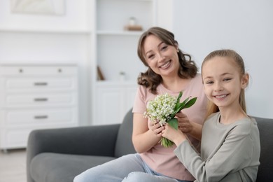 Photo of Girl giving her mother beautiful bouquet of lily-of-the-valley flowers at home. Space for text
