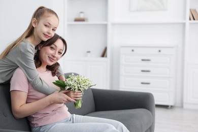 Photo of Girl giving her mother beautiful bouquet of lily-of-the-valley flowers at home. Space for text