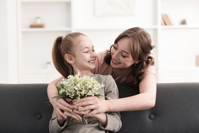 Photo of Girl giving her mother beautiful bouquet of lily-of-the-valley flowers at home
