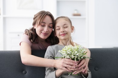 Photo of Girl giving her mother beautiful bouquet of lily-of-the-valley flowers at home