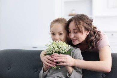 Photo of Girl giving her mother beautiful bouquet of lily-of-the-valley flowers at home. Space for text
