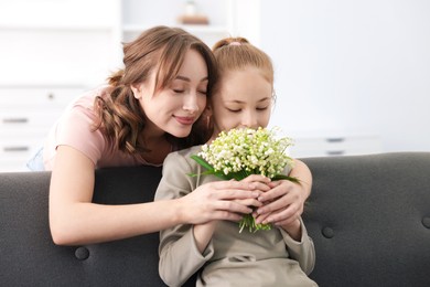 Photo of Girl giving her mother beautiful bouquet of lily-of-the-valley flowers at home