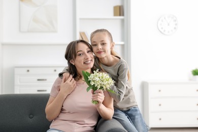 Photo of Girl giving her mother beautiful bouquet of lily-of-the-valley flowers at home