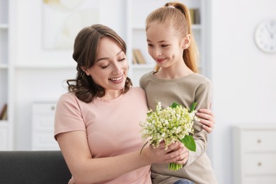 Photo of Girl giving her mother beautiful bouquet of lily-of-the-valley flowers at home