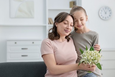 Photo of Girl giving her mother beautiful bouquet of lily-of-the-valley flowers at home. Space for text