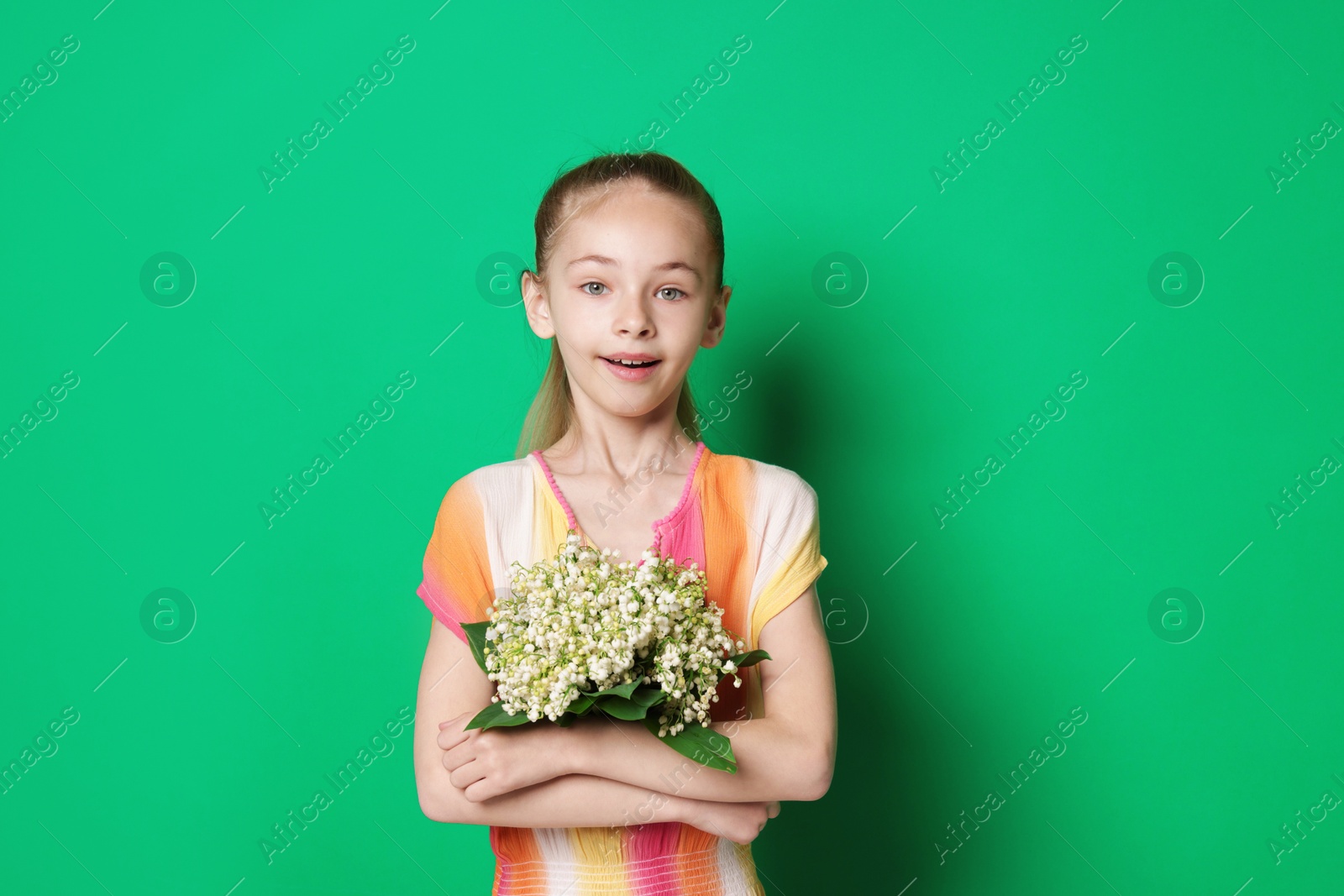 Girl with bouquet of beautiful lily-of-the-valley flowers on green background Photo of Girl with bouquet of beautiful lily-of-the-valley flowers on green background