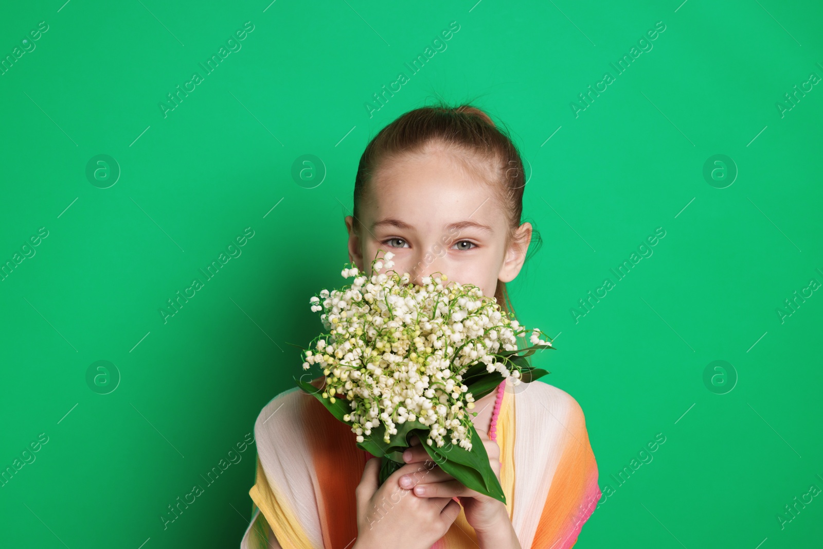 Girl with bouquet of beautiful lily-of-the-valley flowers on green background Photo of Girl with bouquet of beautiful lily-of-the-valley flowers on green background