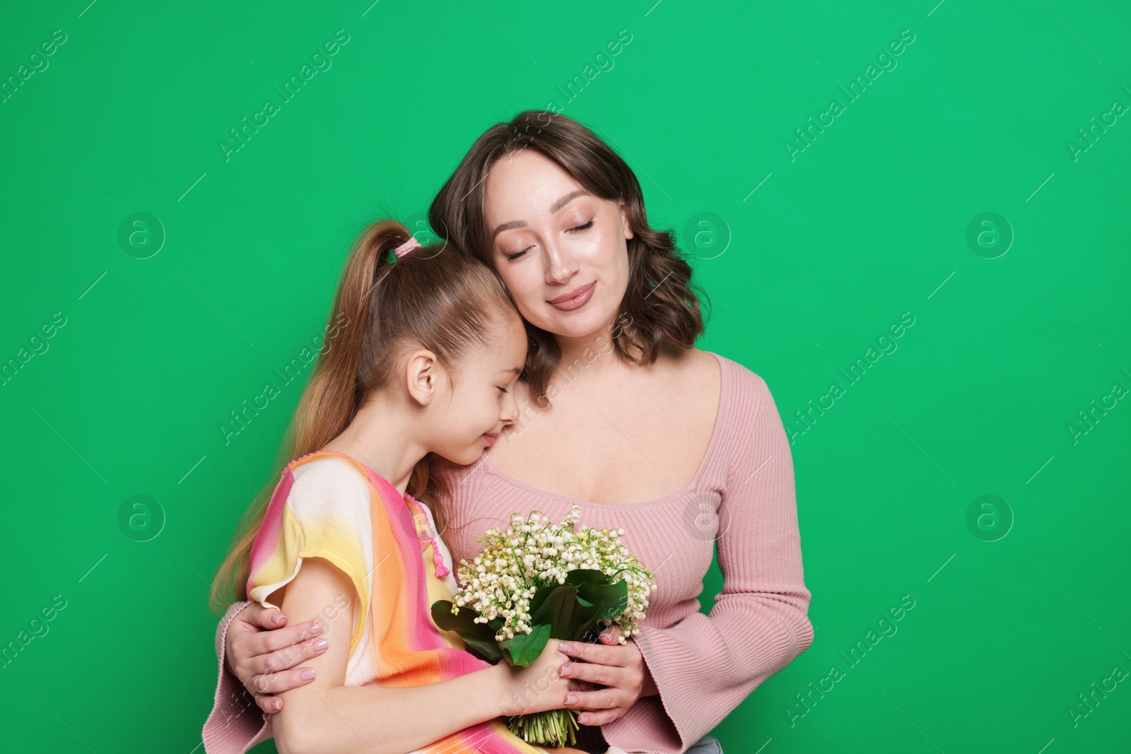 Girl giving her mother beautiful bouquet of lily-of-the-valley flowers on green background Photo of Girl giving her mother beautiful bouquet of lily-of-the-valley flowers on green background