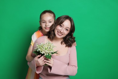 Photo of Girl giving her mother beautiful bouquet of lily-of-the-valley flowers on green background