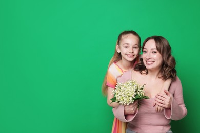Photo of Girl giving her mother beautiful bouquet of lily-of-the-valley flowers on green background. Space for text