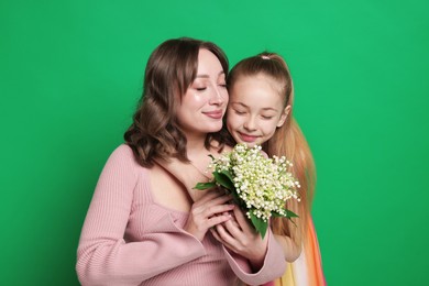 Photo of Girl giving her mother beautiful bouquet of lily-of-the-valley flowers on green background