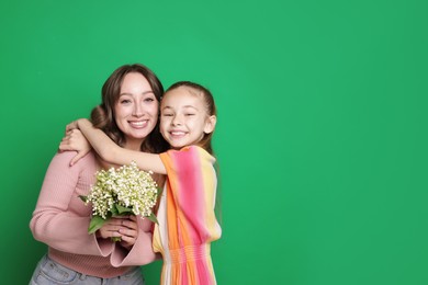 Photo of Girl giving her mother beautiful bouquet of lily-of-the-valley flowers on green background. Space for text