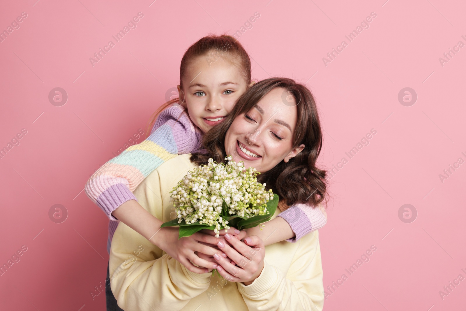Girl giving her mother beautiful bouquet of lily-of-the-valley flowers on light pink background Photo of Girl giving her mother beautiful bouquet of lily-of-the-valley flowers on light pink background
